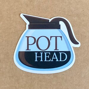 Pode incluir: Um adesivo de cafeteira azul e preto com o texto "POT HEAD" nele.