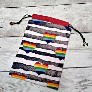 May include: A white drawstring bag with a red top. The bag has a black and white striped pattern with rainbow hearts.