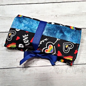 May include: A black fabric roll-up case with a rainbow, heart, and love print. The case is tied with a blue ribbon.