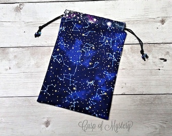 May include: A blue drawstring bag with a constellation print. The bag is made of fabric and has a black drawstring. The bag is on a white wooden surface.