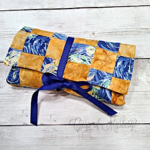 May include: A blue and yellow fabric roll with a blue ribbon tied around it. The fabric has a swirling pattern reminiscent of a famous painting.