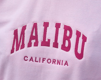 Op de afbeelding: Roze sweatshirt met een roze geborduurde tekst "MALIBU CALIFORNIA".