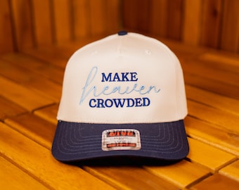May include: A white and navy blue baseball cap featuring the embroidered words "MAKE heaven CROWDED" in light blue. The cap has a curved peak and a structured crown, suitable for casual wear.