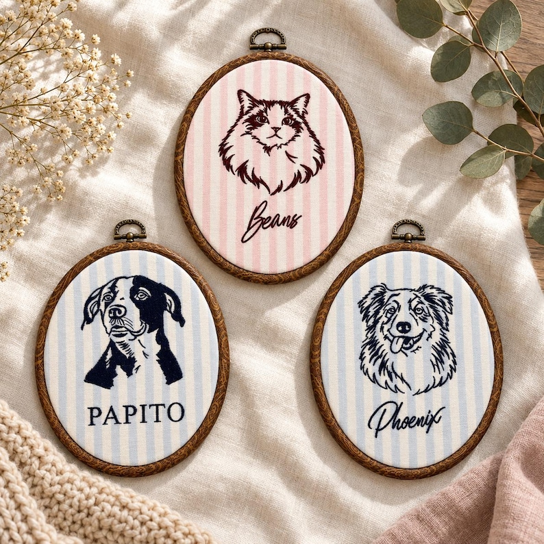 May include: Three oval embroidery hoops featuring fabric portraits of pets. One hoop has a pink striped background with a cat labeled Beans. Two hoops have blue striped backgrounds with dogs labeled PAPITO and Phoenix in dark ink.