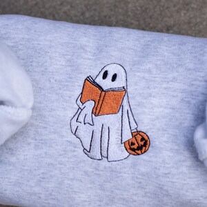 May include: A gray sweatshirt with an embroidered design of a ghost holding a book and a pumpkin.