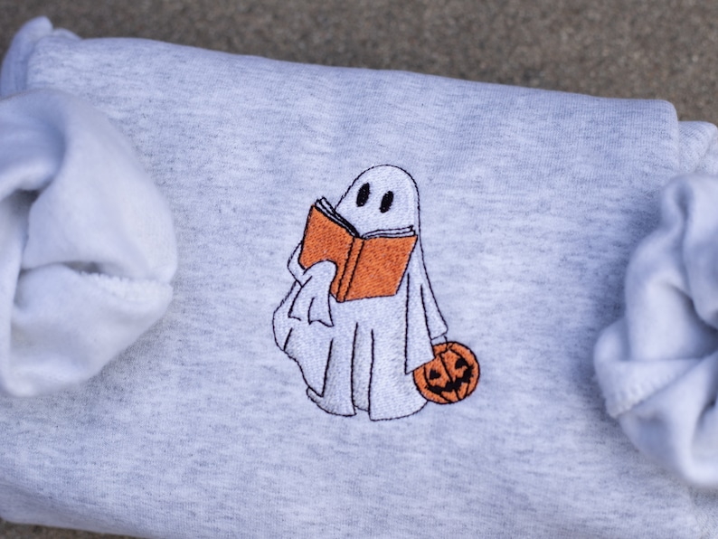 May include: A gray sweatshirt with an embroidered design of a ghost holding a book and a pumpkin.