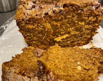 May include: A loaf of pumpkin bread with pecans and a cinnamon streusel topping. The bread is sliced and ready to eat.