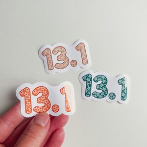 Puede incluir: Tres pegatinas con el texto "13.1". Cada pegatina tiene un borde blanco y un estampado floral dentro de los n&uacute;meros. Una pegatina tiene flores naranjas y melocot&oacute;n, otra tiene flores melocot&oacute;n y la &uacute;ltima tiene flores turquesas.