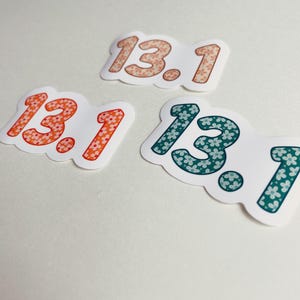 Puede incluir: Tres pegatinas con el n&uacute;mero "13.1" en una fuente redondeada. Las pegatinas son blancas con un estampado floral en naranja, coral y verde azulado. Los n&uacute;meros est&aacute;n delineados en un tono m&aacute;s oscuro del mismo color.