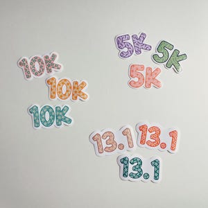 Puede incluir: Una colecci&oacute;n de pegatinas coloridas con los n&uacute;meros "10K", "5K" y "13.1" en varios dise&ntilde;os. Las pegatinas presentan patrones florales y de hojas en tonos de rosa, naranja, verde y morado, con un borde blanco. Ideal para corredores.