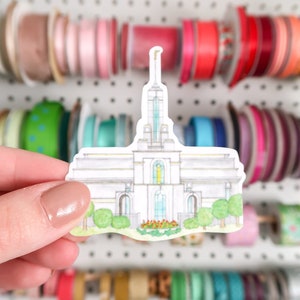 May include: A white watercolor illustration of a temple with a gold spire. The temple has a green lawn and red flowers in front of it.