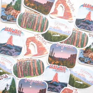 Pode incluir: Uma cole&ccedil;&atilde;o de adesivos coloridos que representam v&aacute;rios parques nacionais e monumentos. Os adesivos s&atilde;o impressos com ilustra&ccedil;&otilde;es de locais emblem&aacute;ticos como o Parque Nacional Arches, o Parque Nacional Yosemite e o Parque Nacional dos Vulc&otilde;es do Hava&iacute;. Cada adesivo tem o nome do parque e sua localiza&ccedil;&atilde;o.