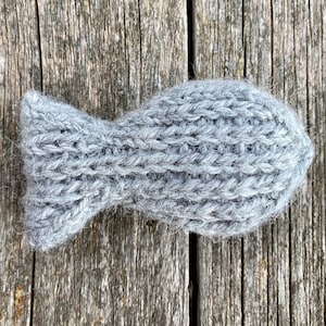 May include: A gray knitted fish toy. The fish is made of a soft, fuzzy yarn and has a simple, classic design.