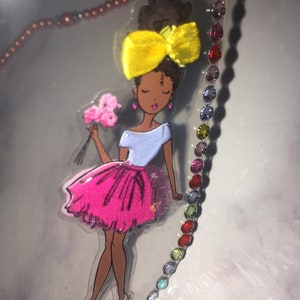May include: A colorful sticker of a cartoon girl with brown skin, wearing a pink skirt, a blue shirt, and a yellow bow in her hair. She is holding a bouquet of pink flowers.