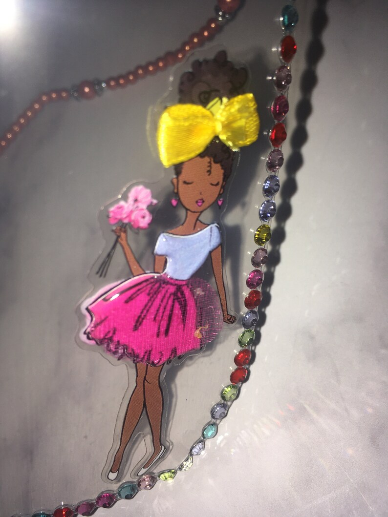 May include: A colorful sticker of a cartoon girl with brown skin, wearing a pink skirt, a blue shirt, and a yellow bow in her hair. She is holding a bouquet of pink flowers.