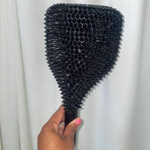 May include: A black massage tool with a textured surface covered in small, sharp spikes. The tool has a long, cylindrical handle. The tool is held by a person.
