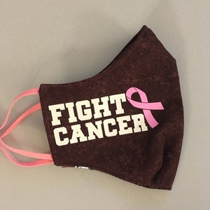 May include: Brown fabric face mask with the text "FIGHT CANCER" in white and a pink ribbon.