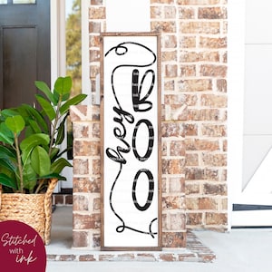 Peut inclure: Une pancarte en bois avec un fond blanc et des lettres noires qui disent "Hey Boo". La pancarte est accrochée à un mur en briques.