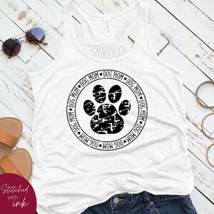 Op de afbeelding: Een wit tanktop met een zwarte poot afdruk en de tekst "Dog Mom" die herhaald wordt rond de afdruk.