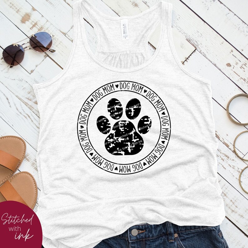 Op de afbeelding: Een wit tanktop met een zwarte poot afdruk en de tekst "Dog Mom" die herhaald wordt rond de afdruk.