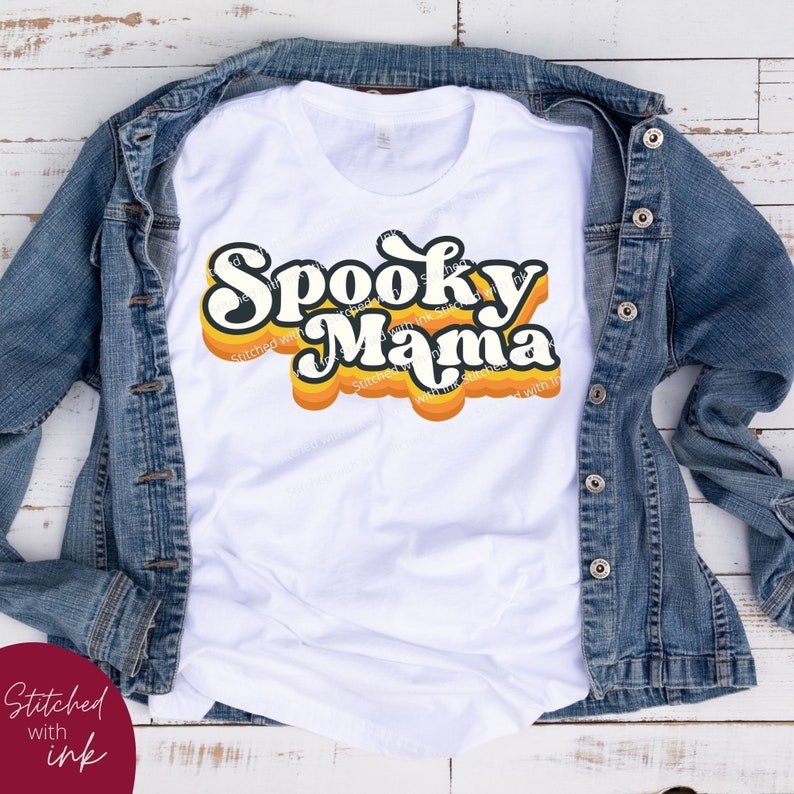 May include: White t-shirt with a retro-style graphic that says "Spooky Mama" in orange and black letters.
