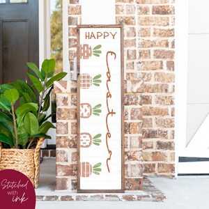 May include: A white wooden sign with the text "Happy Easter" written in brown cursive script. The sign is decorated with five brown and orange carrots with green leaves.