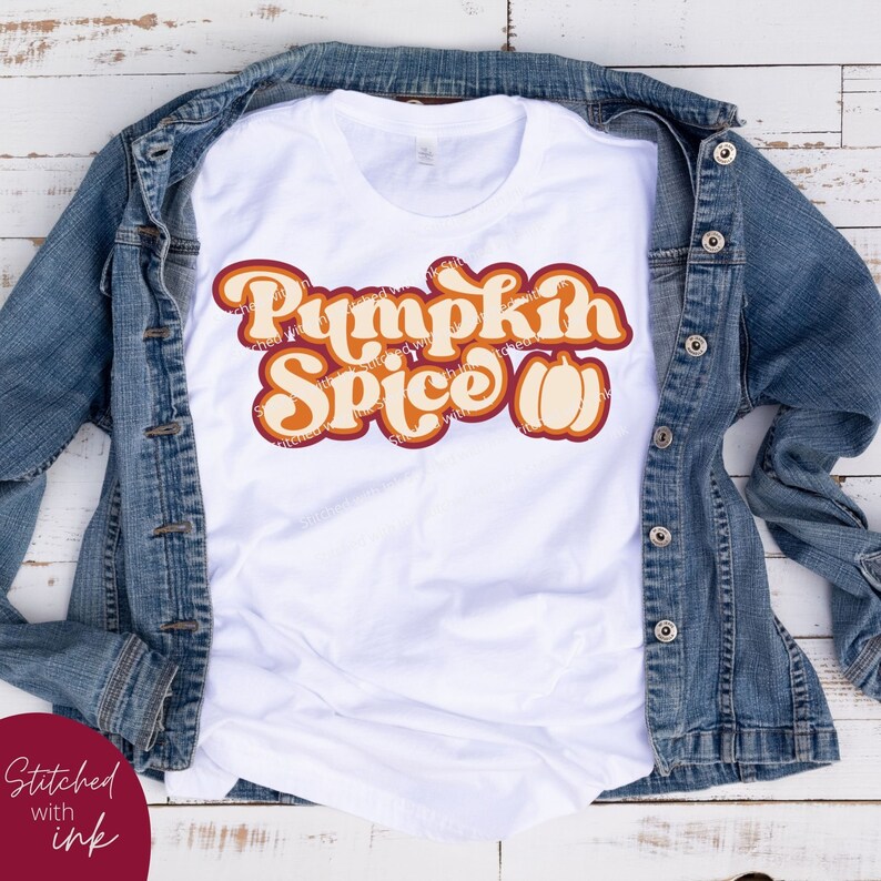 May include: White t-shirt featuring a retro-style graphic that reads "Pumpkin Spice" in orange and red lettering with a stylised orange pumpkin.