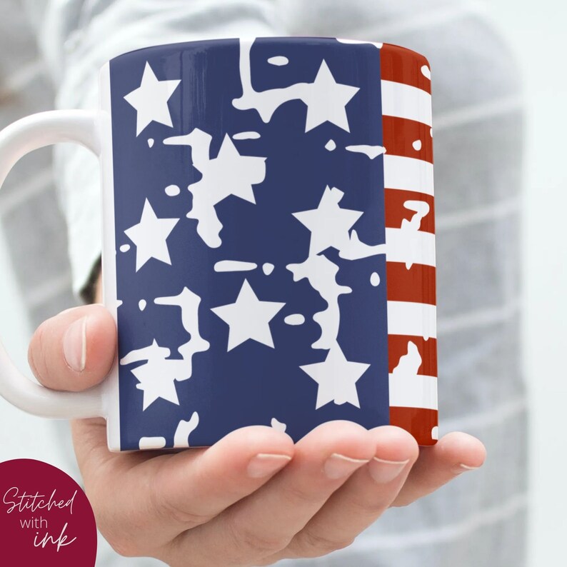 K&ouml;nnte beinhalten: Eine wei&szlig;e Keramiktasse mit einem amerikanischen Flaggenmuster in Blau und Rot. Das Flaggenmuster zeigt wei&szlig;e Sterne auf blauem Hintergrund und rote und wei&szlig;e Streifen.