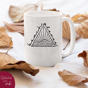 K&ouml;nnte beinhalten: Wei&szlig;e Keramiktasse mit einer schwarzen Linienzeichnung eines Dreiecks, um das herum das Wort "peace" geschrieben ist. Das Dreieck enth&auml;lt eine Sonne mit Strahlen und wellenf&ouml;rmige Linien, die Wasser darstellen.
