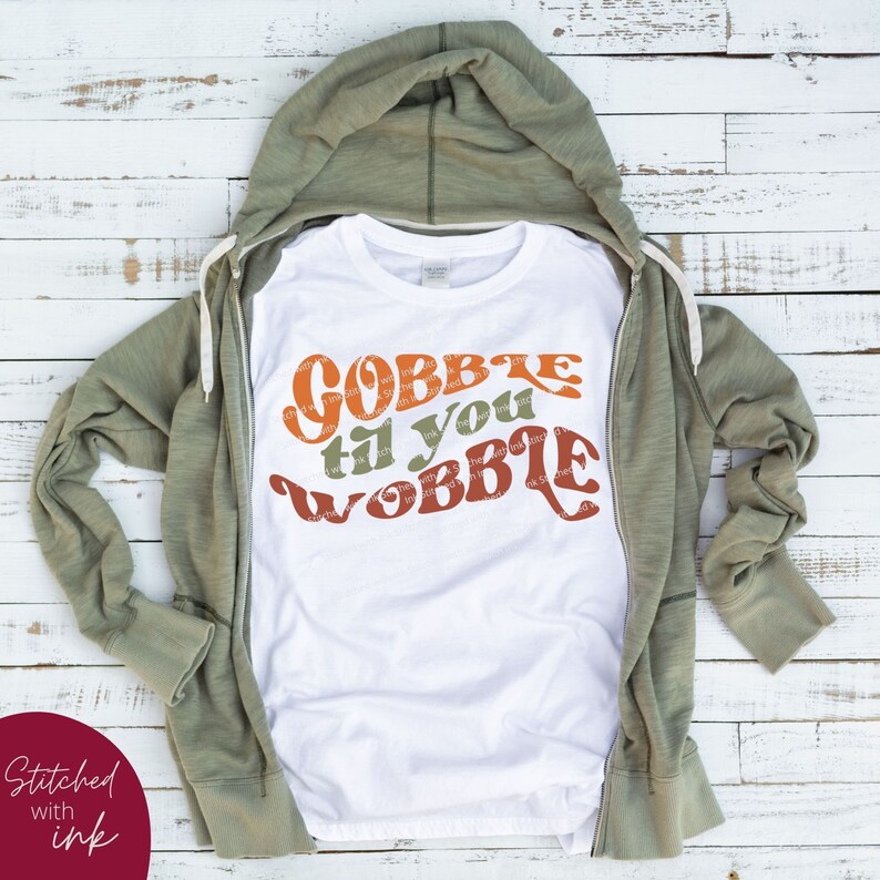 May include: White t-shirt with a retro-style graphic that says "Gobble til you wobble" in orange, brown, and green.