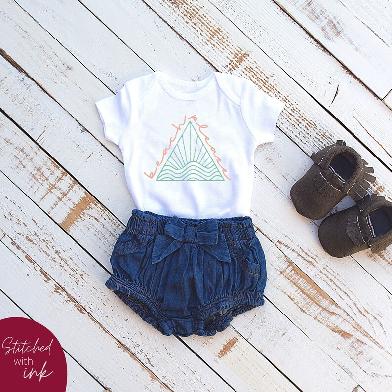 K&ouml;nnte beinhalten: Ein wei&szlig;er Baby-Strampler mit einem gr&uuml;nen Dreiecks-Motiv, auf dem "beach vibes" in einem pfirsichfarbenen Orange steht. Der Strampler wird mit Jeans-Shorts und braunen Mokassins kombiniert.