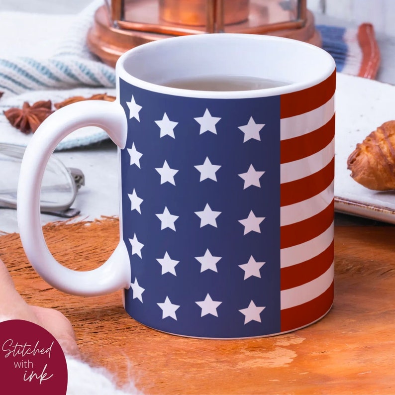 K&ouml;nnte beinhalten: Eine wei&szlig;e Keramiktasse mit einem amerikanischen Flaggenmuster in Blau und Rot. Die Tasse ist mit einer hellbraunen Fl&uuml;ssigkeit gef&uuml;llt.