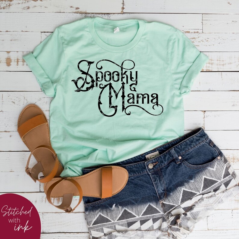 May include: A light green t-shirt with a black graphic that says "Spooky Mama" in a decorative font.
