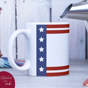 K&ouml;nnte beinhalten: Wei&szlig;e Keramiktasse mit einem amerikanischen Flaggenmuster in Blau und Rot. Die Tasse hat ein wei&szlig;es Innenleben und einen gro&szlig;en Henkel.