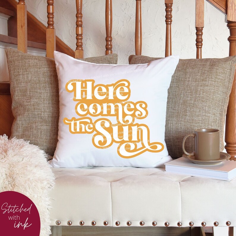 May include: White throw pillow with the text "Here comes the sun" in a retro, orange font.