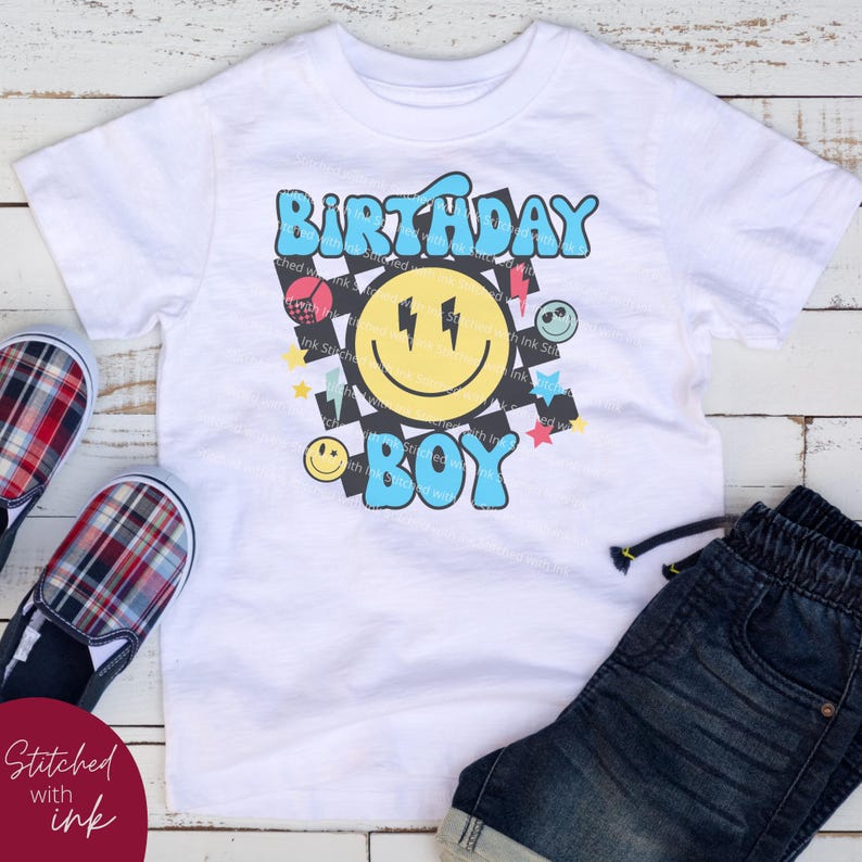 May include: White t-shirt with a blue and yellow smiley face graphic, black and white checkered background, and the text "Birthday Boy".