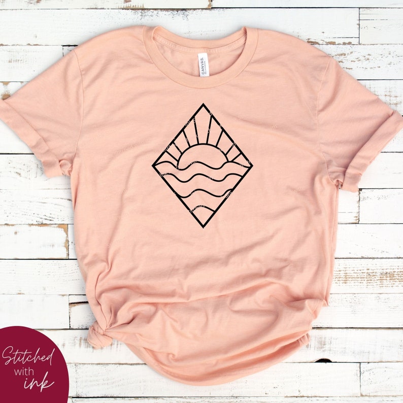 May include: A peach-colored t-shirt with a black graphic of a sun setting over wavy water inside a diamond shape.