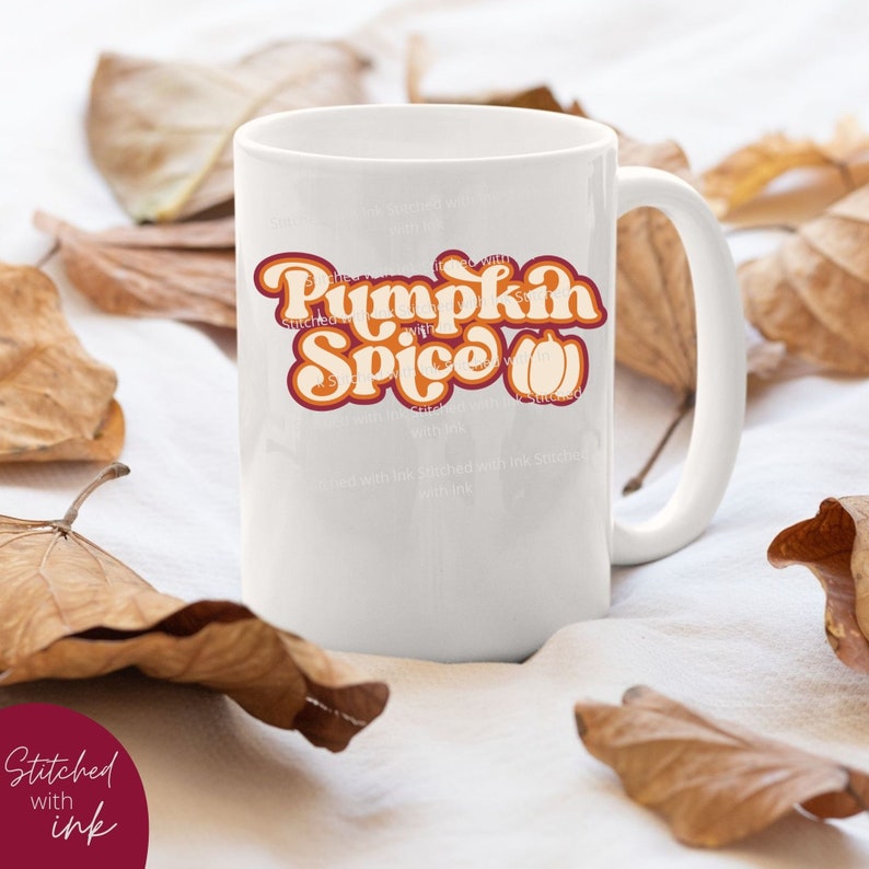 May include: White ceramic mug featuring a graphic design that reads "Pumpkin Spice" in a retro font with an orange pumpkin graphic. The mug is placed on a white surface with brown leaves.