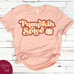 May include: A peach-coloured t-shirt with the text "Pumpkin Spice" in a retro font with a pumpkin graphic.