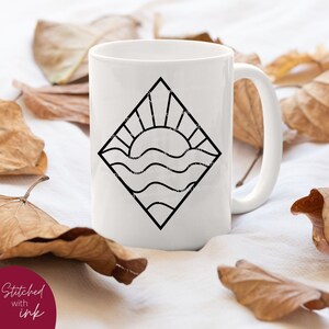 May include: White ceramic mug with a black line drawing of a sun setting over waves inside a diamond shape.