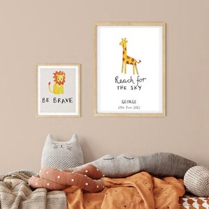 Może przedstawiać: Dwa oprawione wydruki z ilustracjami zwierząt i inspirującym tekstem. Pierwszy wydruk przedstawia lwa z tekstem "Be Brave". Drugi wydruk przedstawia żyrafę z tekstem "Reach for the Sky" oraz imieniem "George" i datą "23rd June 2023".