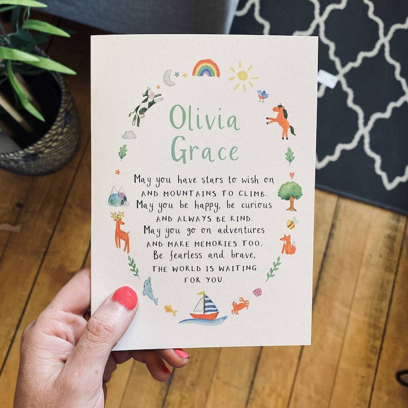 May include: A white card with a colourful illustration of animals and nature surrounding the text "Olivia Grace". The text reads "May you have stars to wish on and mountains to climb. May you be happy, be curious and always be kind. May you go on adventures and make memories too. Be fearless and brave, the world is waiting for you."