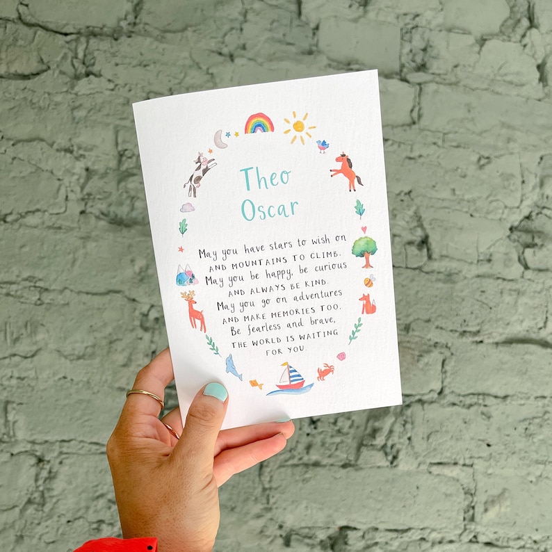 May include: A white card with a colourful illustration of animals and nature surrounding the names Theo Oscar. The card has a message wishing the child well in life with wishes for happiness, kindness, and adventure.