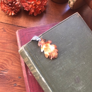 May include: A green and red book with a copper leaf bookmark. The bookmark is shaped like an oak leaf and has a textured surface.