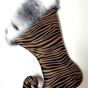 May include: A Christmas stocking with a tiger stripe pattern in brown and black. The top of the stocking is trimmed with white and grey faux fur. The stocking has a curled toe.