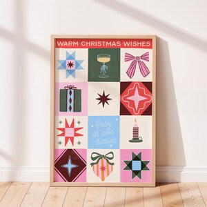 Op de afbeelding: Een ingelijste print met een feestelijk ontwerp. Het kunstwerk toont een raster van kleurrijke vierkanten met kerstthema-illustraties, waaronder sterren, cadeaus en een champagneglas. De tekst "Warm Christmas Wishes" staat bovenaan en "Baby it's cold Outside" in het midden.