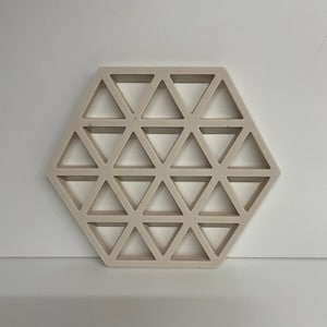 Könnte beinhalten: Ein sechseckiger Untersetzer aus beigefarbenem Beton mit einem geometrischen Muster aus Dreiecken.