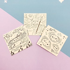 May include: Three black and white illustrations of frogs and lily pads. The first illustration shows a frog sitting on a lily pad with a single leaf. The second illustration shows a frog sitting on a lily pad with multiple leaves. The third illustration shows a frog sitting on a lily pad with a single leaf and a single stem.