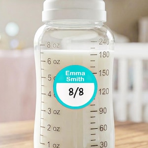 May include: A clear plastic baby bottle with a white cap and measurement markings in ounces and milliliters. A circular teal and white sticker is applied to the front, featuring the name Emma Smith and the handwritten date 8/8 in black ink.
