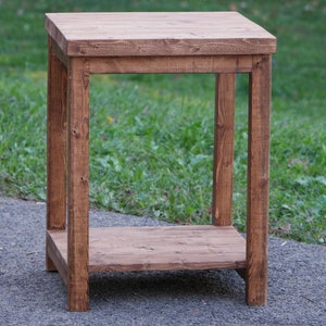 May include: A rustic wooden end table with a single shelf. The table is made of natural wood with a dark brown stain. It has a simple design with straight legs and a rectangular top.